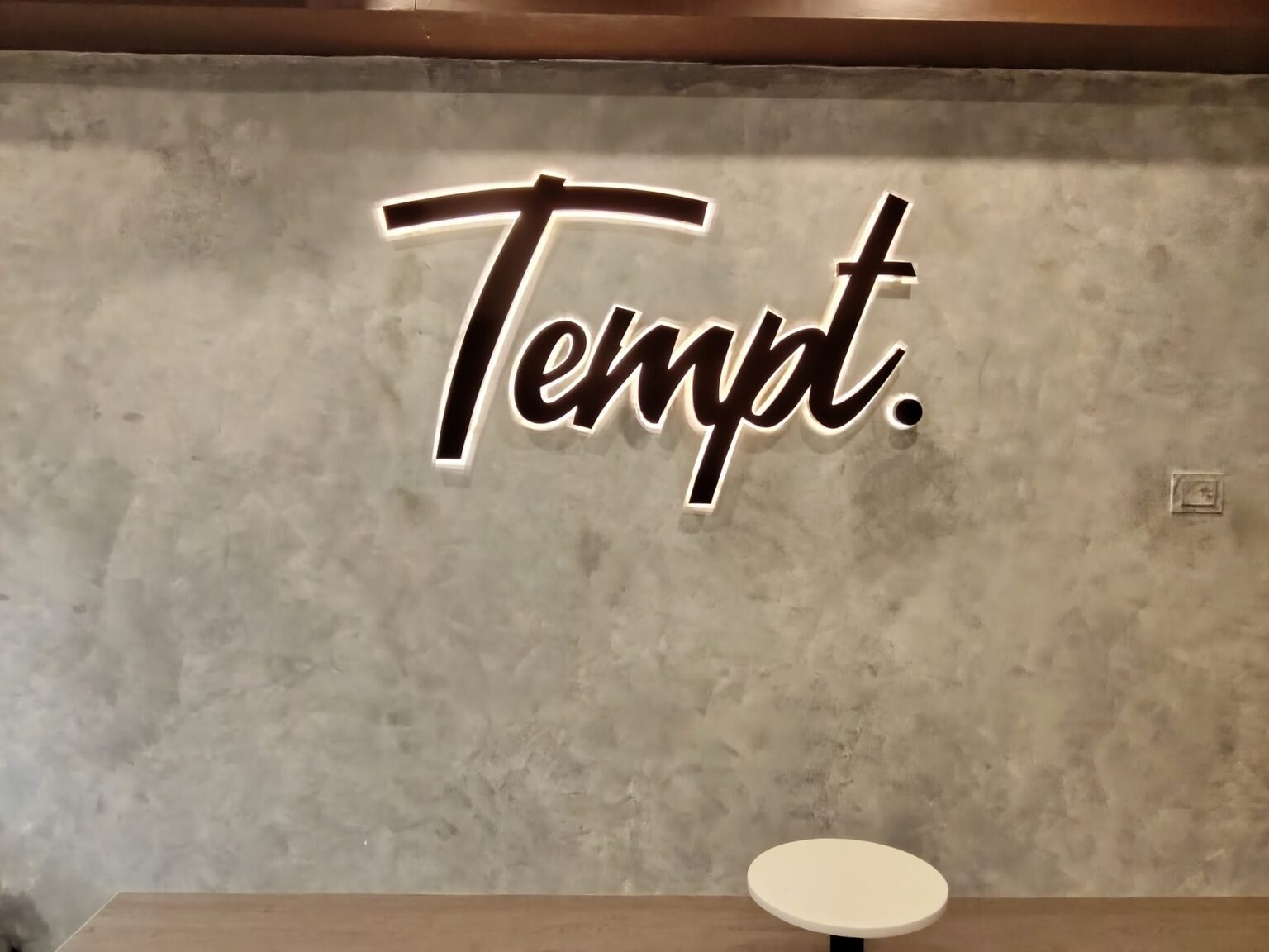Tempt. 3D bronze lettering on a raw concrete interior wall