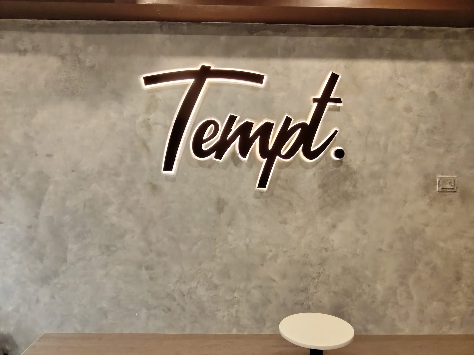 Tempt. 3D bronze lettering on a raw concrete interior wall